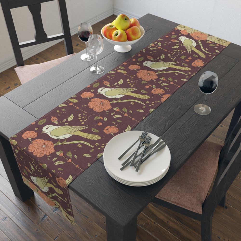 Dining table set with a decorative table runner featuring birds and flowers in rich, warm fall tones