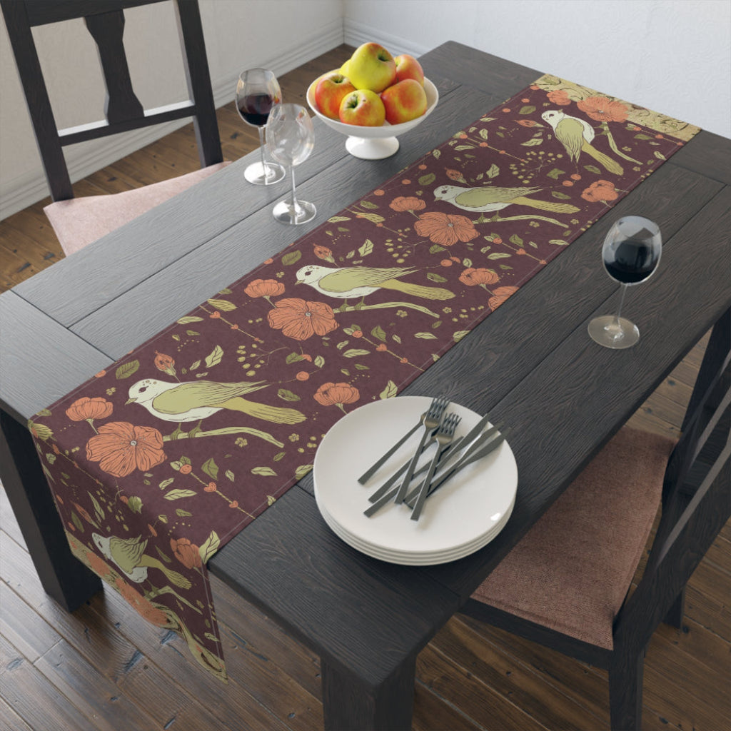 Dining table set with a decorative table runner featuring birds and flowers in rich, warm fall tones