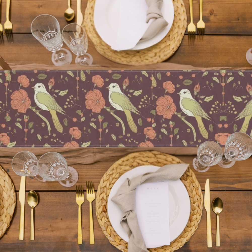 Table runner with birds and flowers in rich autumn tones shown in a festive table setting with gold flatware and wicker plate chargers