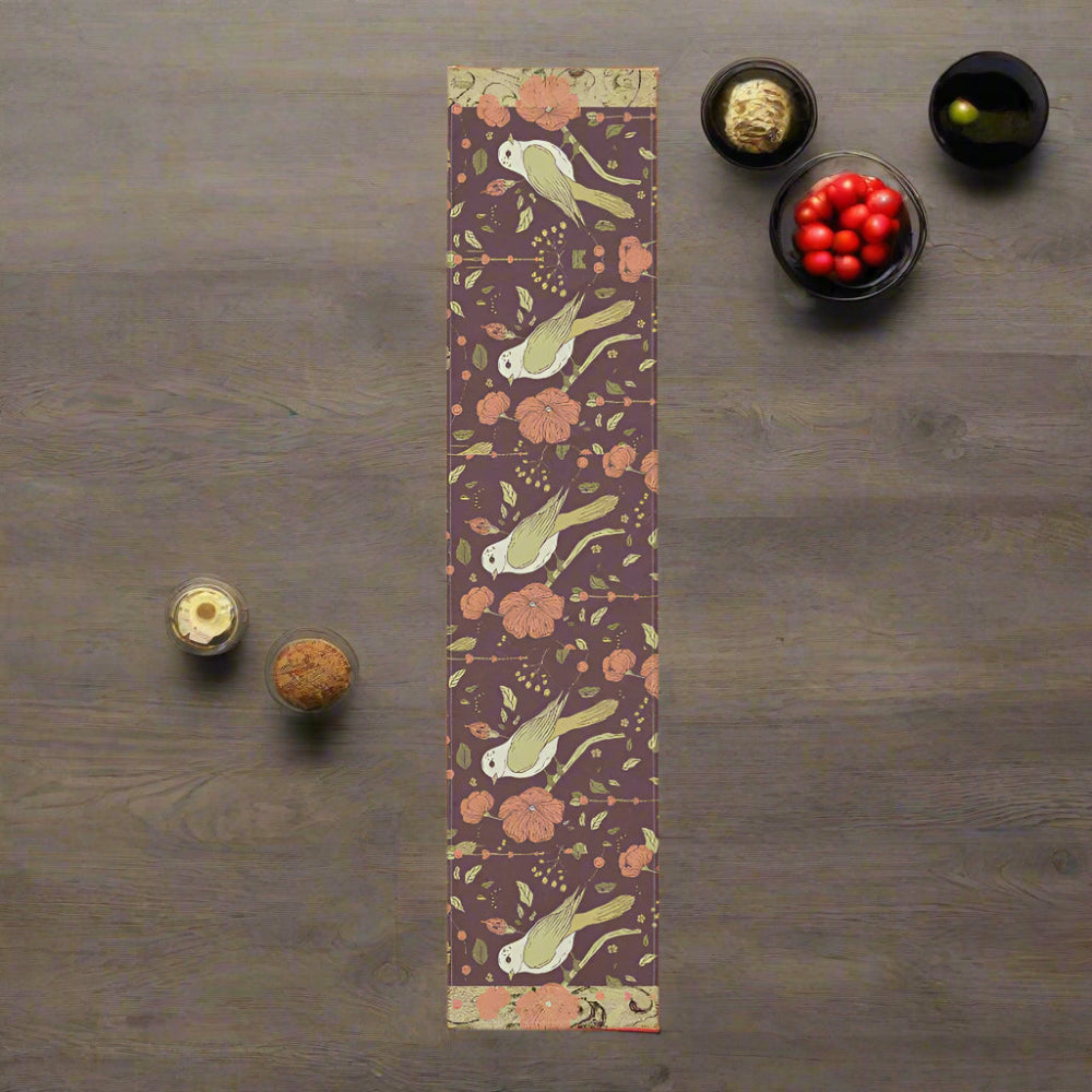 Table runner with birds and flowers in rich autumn tones shown on a wood background with kitchen items