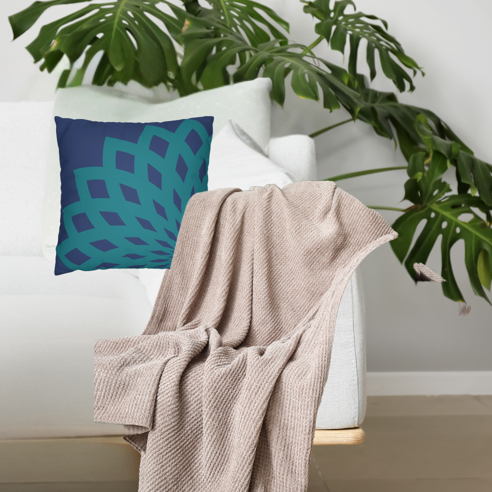 A dark blue pillow with a teal floral pattern shown on a white couch with a throw