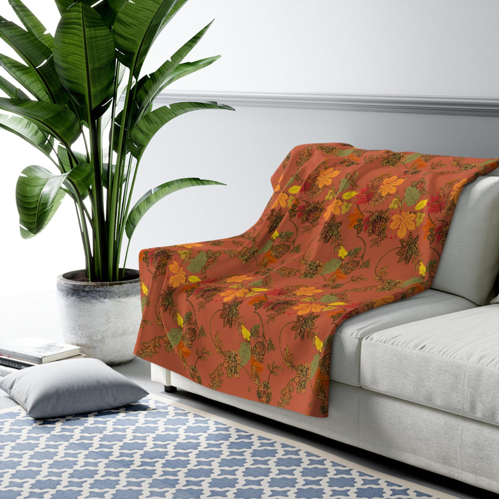 Floral-patterned orange blanket with green and yellow leaves draped over a white sofa in a living room setting with a plant and rug.