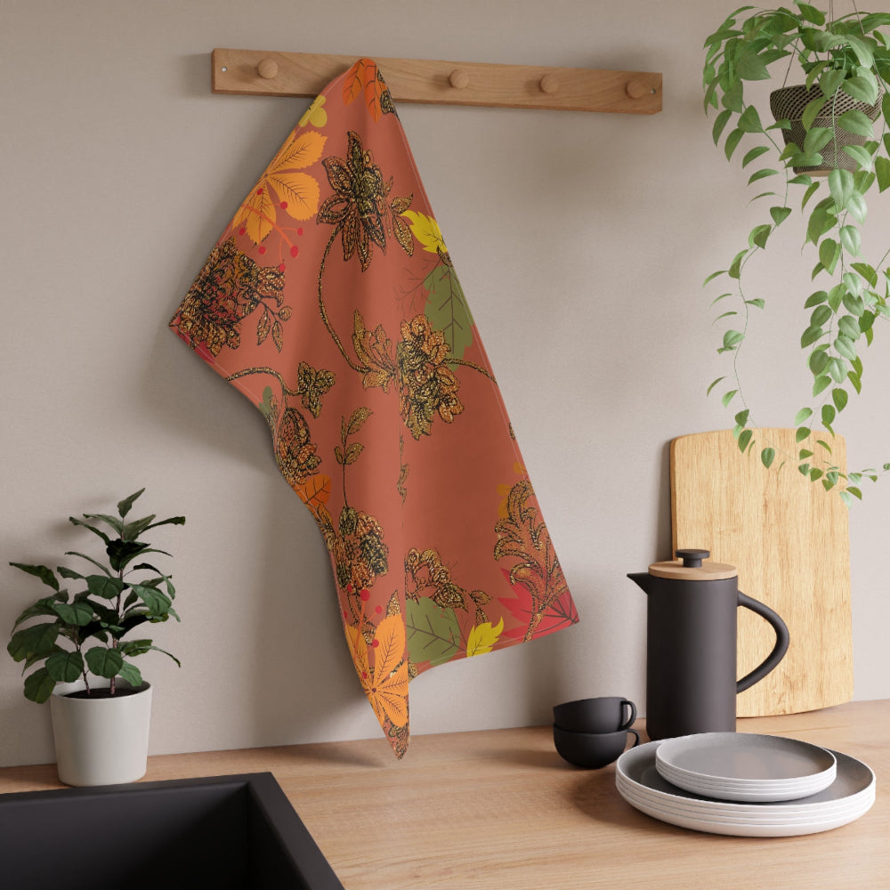 Fall floral towel hanging on a wooden rack with kitchen items and plants in the background.