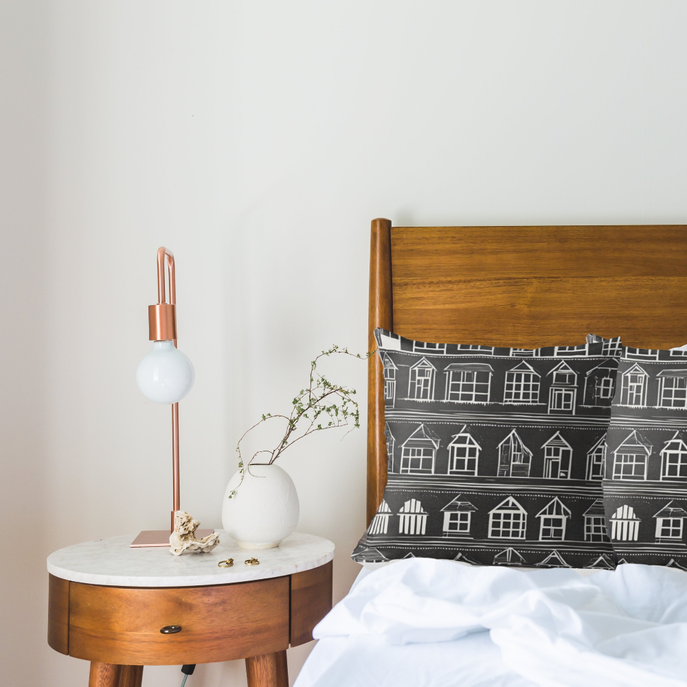 Wooden headboard with Home Sweet Home patterned pillow next to a nightstand with lamp and vase.