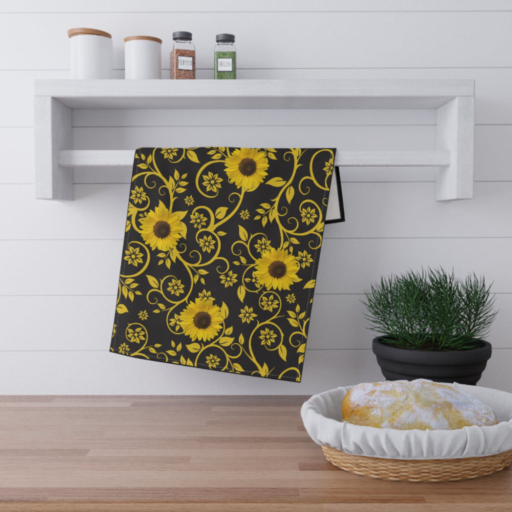 Black towel with yellow sunflower pattern on a wooden surface with a plant and basket in the background.
