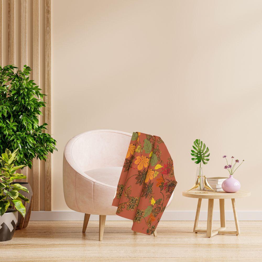 Rich, autumn toned blanket with leaf pattern shown on a round upholstered chair in a contemporary room