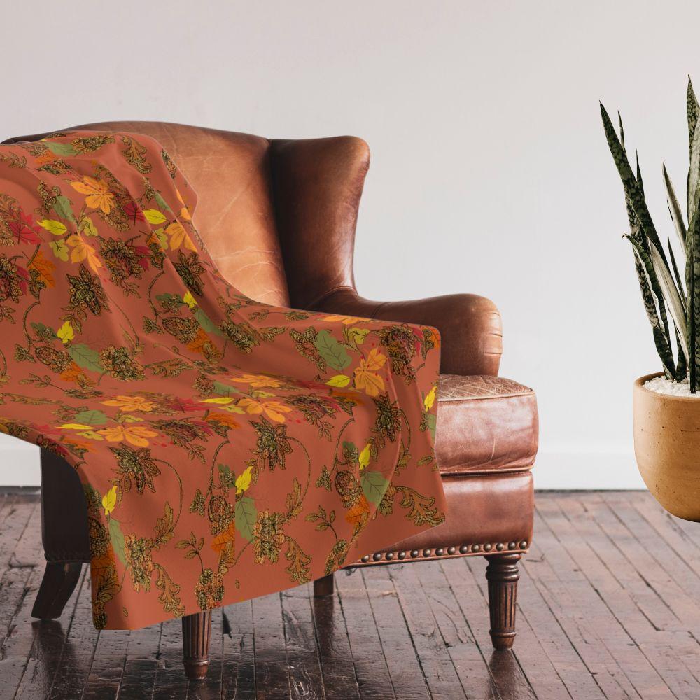 Rich, autumn toned blanket with leaf pattern shown on a leather arm chair
