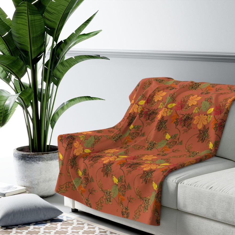 Rich, autumn toned blanket with leaf pattern shown on a sofa in a living room