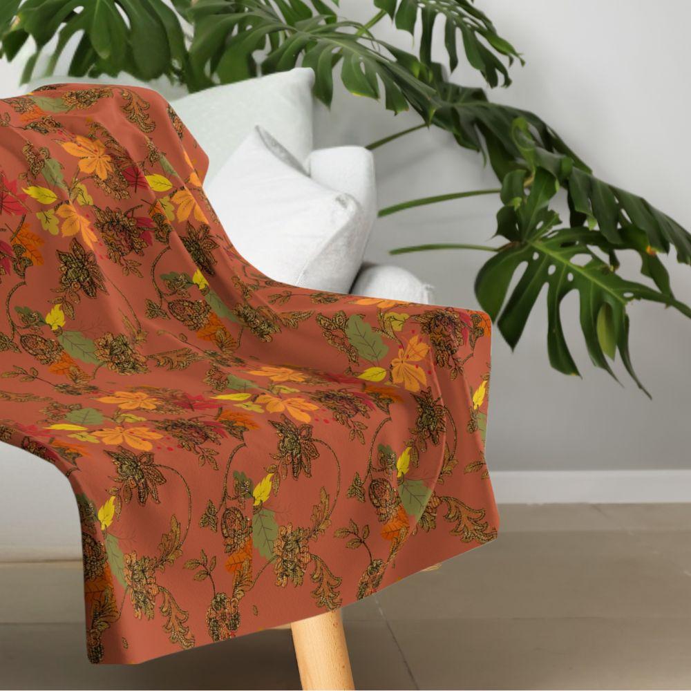 Rich, autumn toned blanket with leaf pattern shown on a contemporary white sofa