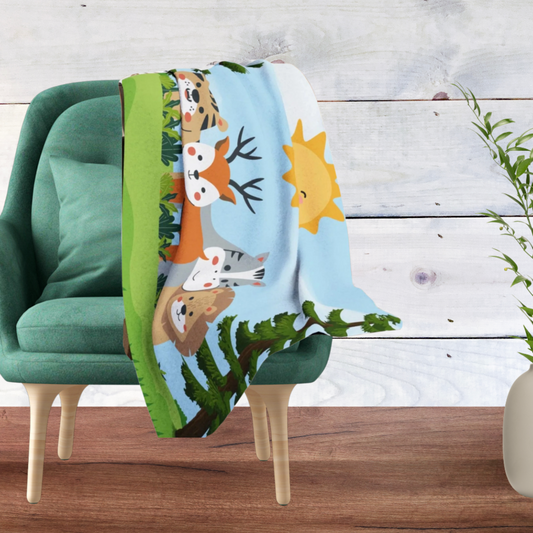 A colorful throw blanket featuring cartoon forest animals and a sun, draped over a green armchair in a styled room setting with a wood plank wall and floor.