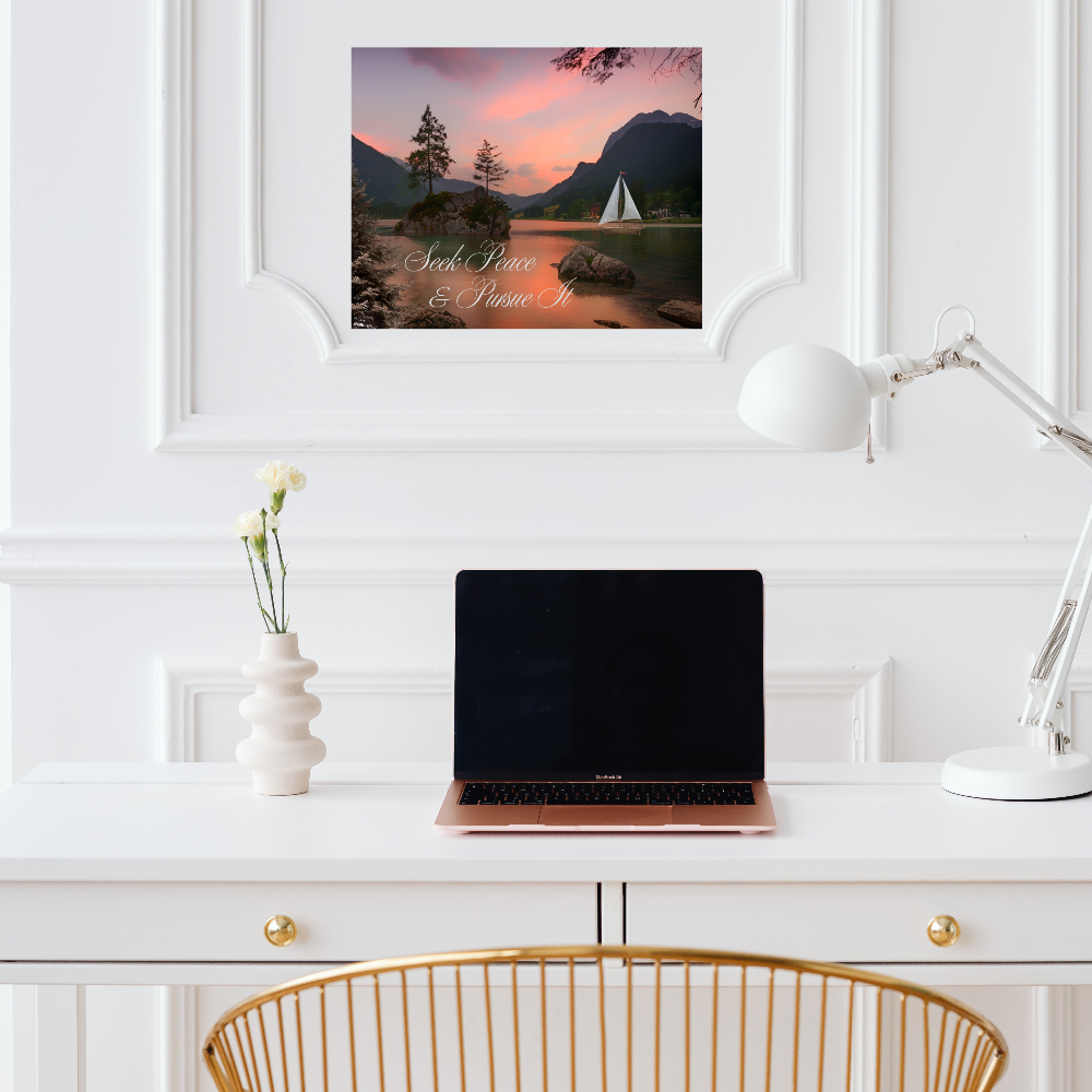 Home office setup with a laptop, lamp, and canvas print with text Seek Peace and Pursue it shown above a white desk.