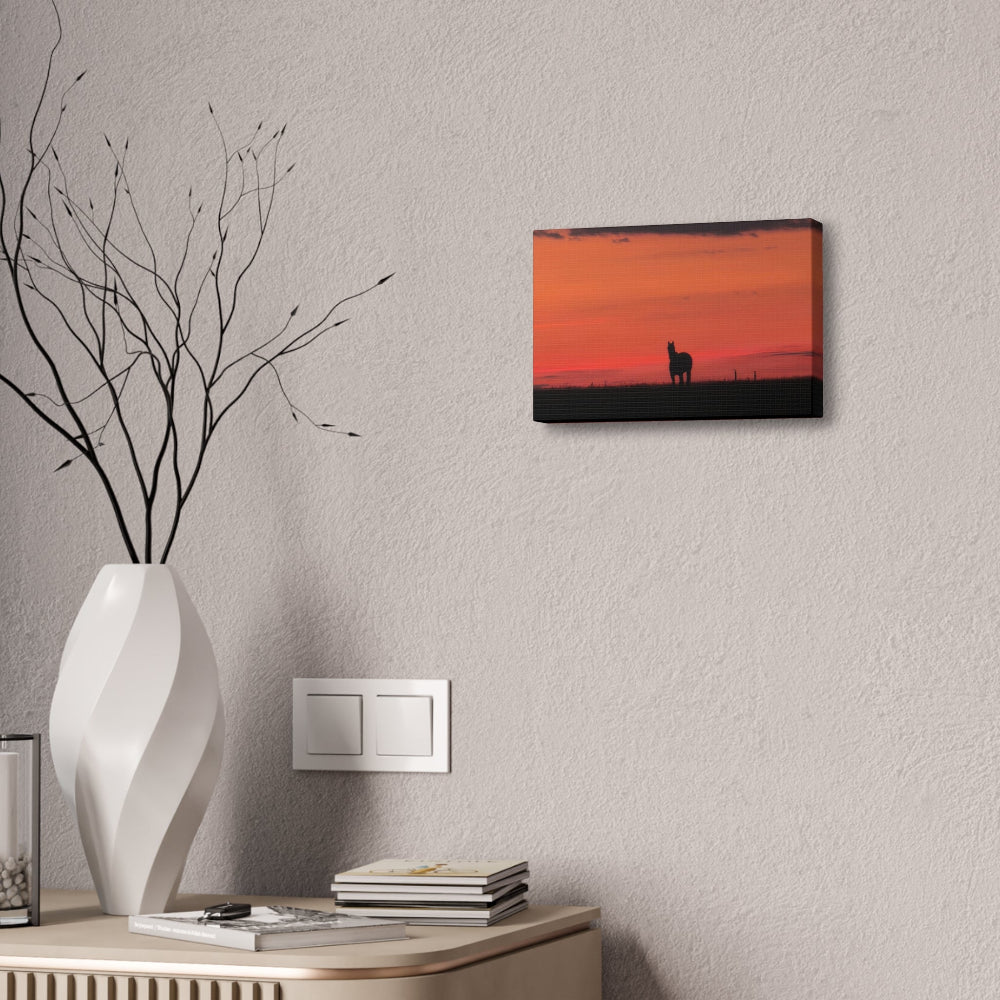 Decorative setup with a vase, books, and a wall art piece of a sunset  horse silhouette on a gray wall.