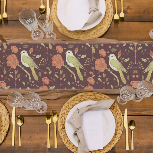 Table runner with birds and flowers in rich autumn tones shown in a festive table setting with gold flatware and wicker plate chargers