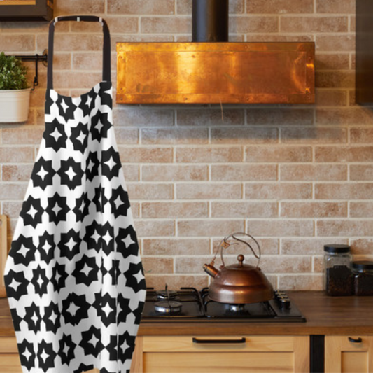 A black and white farmhouse style apron with geometric print shown hanging next to an elegant copper range hood/vent 