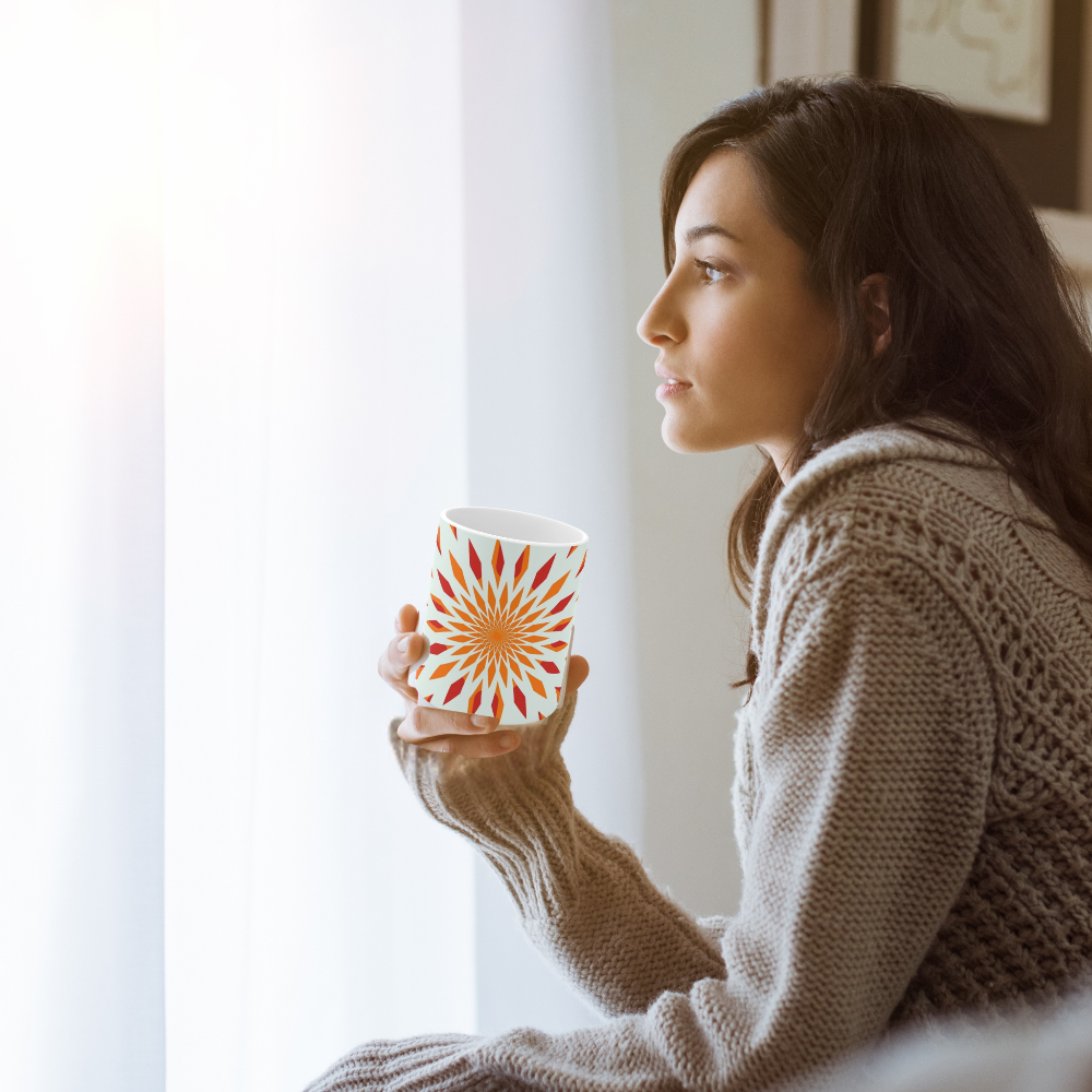 orange starburst mug shown with a woman holding it and looking out of a window