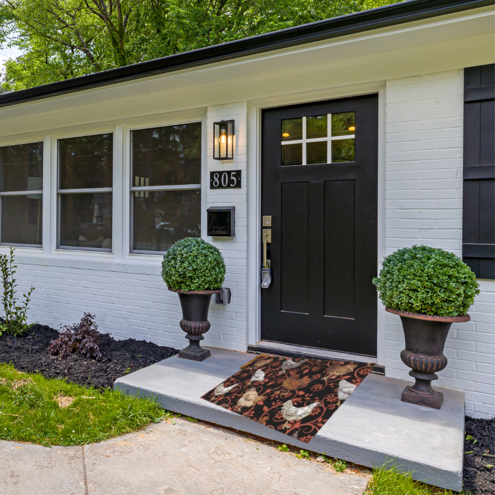 Chicken Outdoor Rug shown in front of a white house with a black door and trim