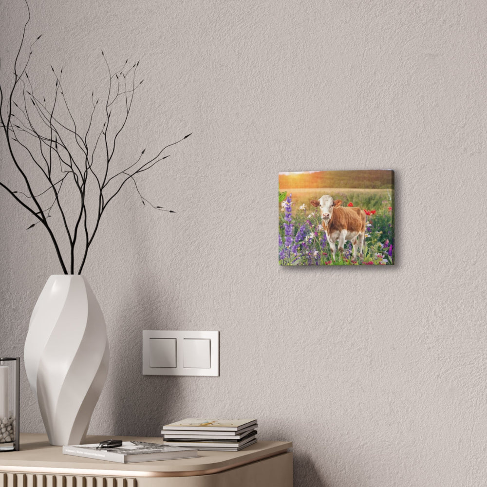 Canvas print of a cow in a field hanging on a wall above a desk with decorative items.