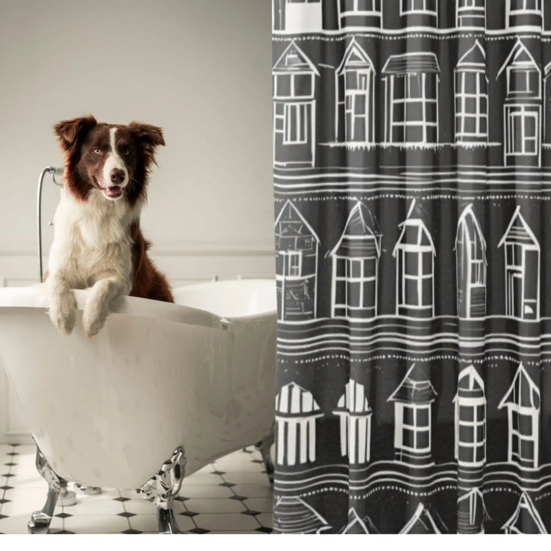 A dog sitting in a white clawfoot bathtub next to a black shower curtain printed with white house outlines, in a bathroom setting.