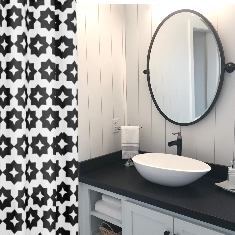 A black and white geometric patterned shower curtain shown in a black and white bathroom