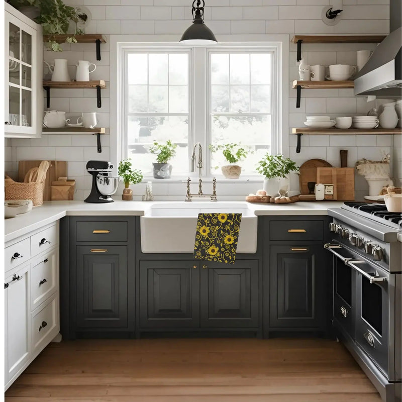 A bright, modern farmhouse-style kitchen with dark charcoal gray cabinets, white subway tile, a white farmhouse sink, open wood shelves, and a yellow sunflower-patterned towel hanging over the sink.