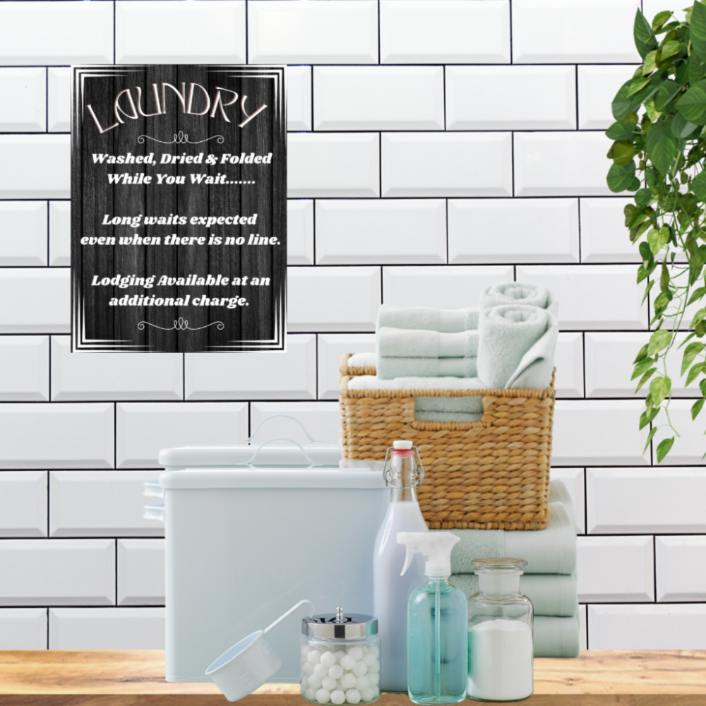 Laundry area with a basket of towels, cleaning supplies, and a humorous laundry sign on a tiled wall.