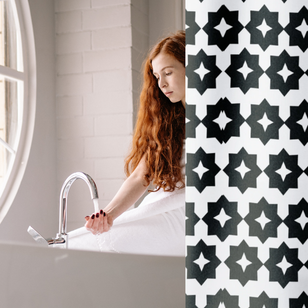 A black and white geometric patterned shower curtain shown in an elegant bathroom with a female model