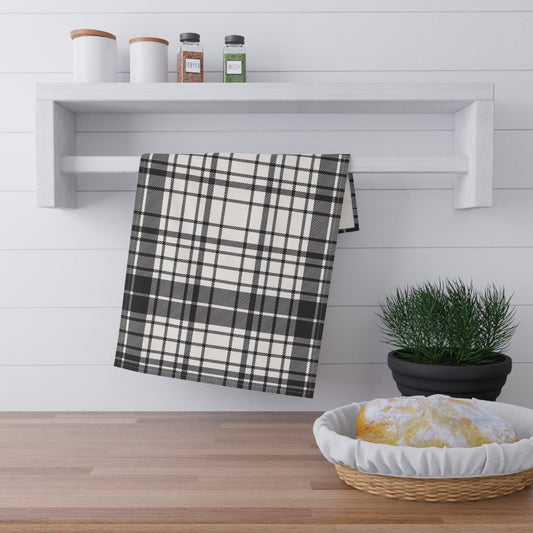  A crisp black and white plaid towel hanging on a white shelf with a plant and basket in the foreground.