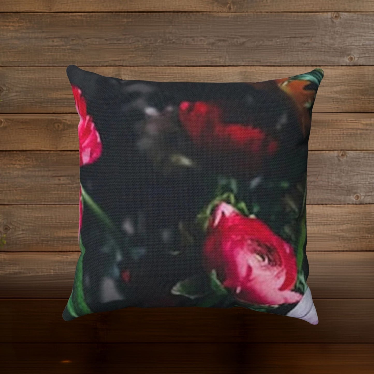 A square throw pillow featuring a dark floral print with prominent pink and red peony flowers, set against a rustic brown wooden plank background.