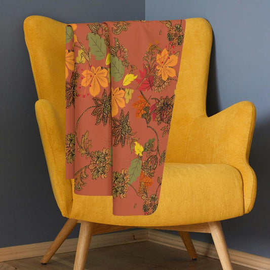 Rich, autumn toned blanket with leaf pattern shown on a gold suede chair in a blue room.
