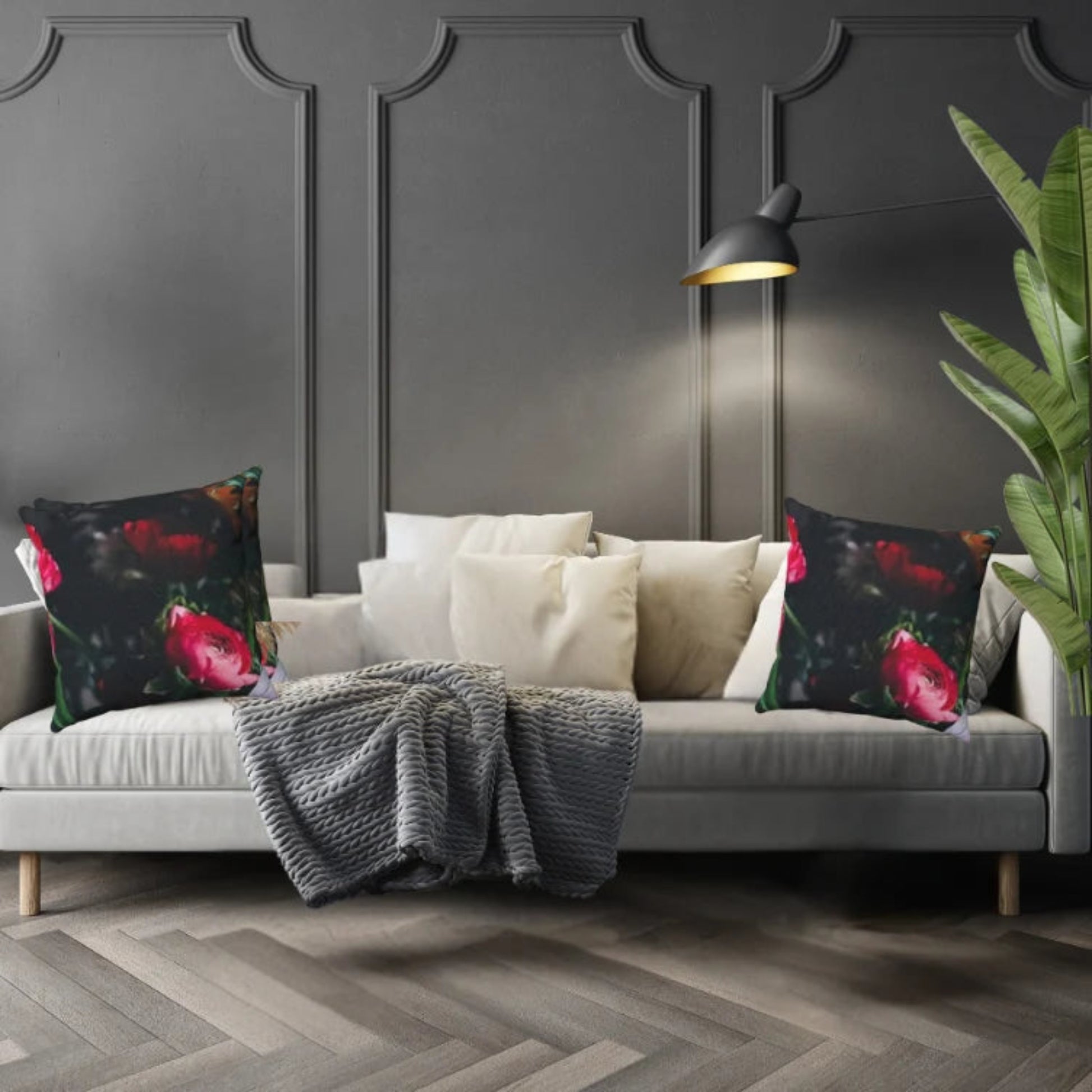 Dark floral pillows shown on a gray sofa with a blanket against a dark paneled wall.